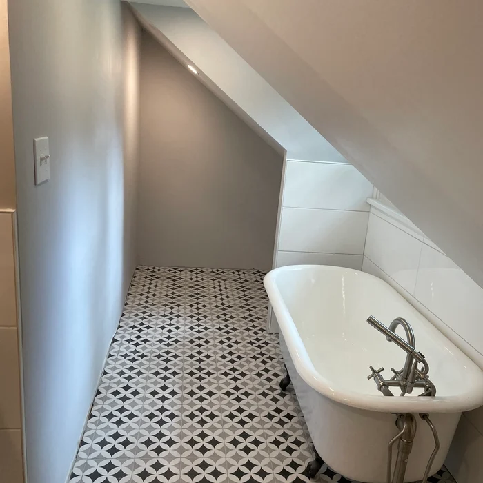 White claw-foot bathtub beneath a sloping ceiling beside a patterned bathroom floor.