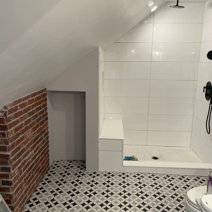 Separate tiled shower with a black showerhead beneath the attic bathroom’s sloping ceiling.