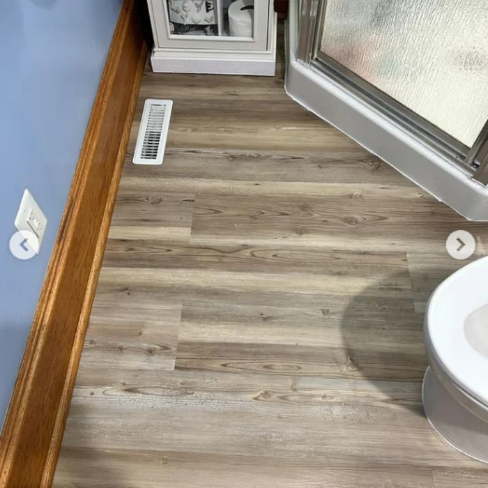 Wood-look floor fitted around the same corner shower, with the floor vent visible.