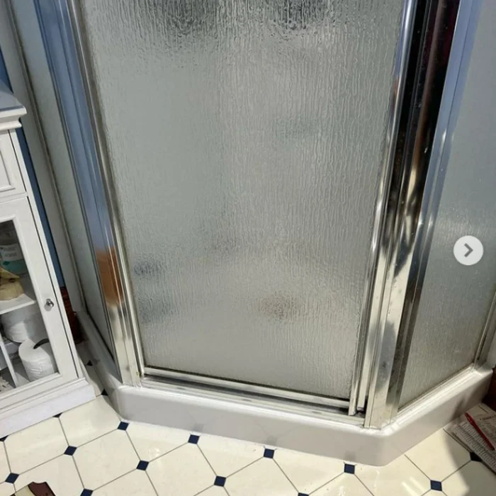 Original patterned floor beside a frosted-glass corner shower and blue bathroom walls.