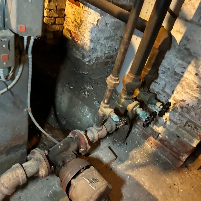Existing heating pipes, valves and a circulating pump beside the basement wall.