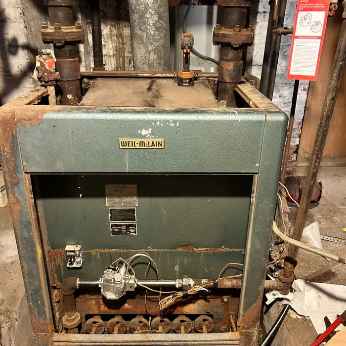 Large original cast-iron boiler in a brick-walled basement mechanical area.