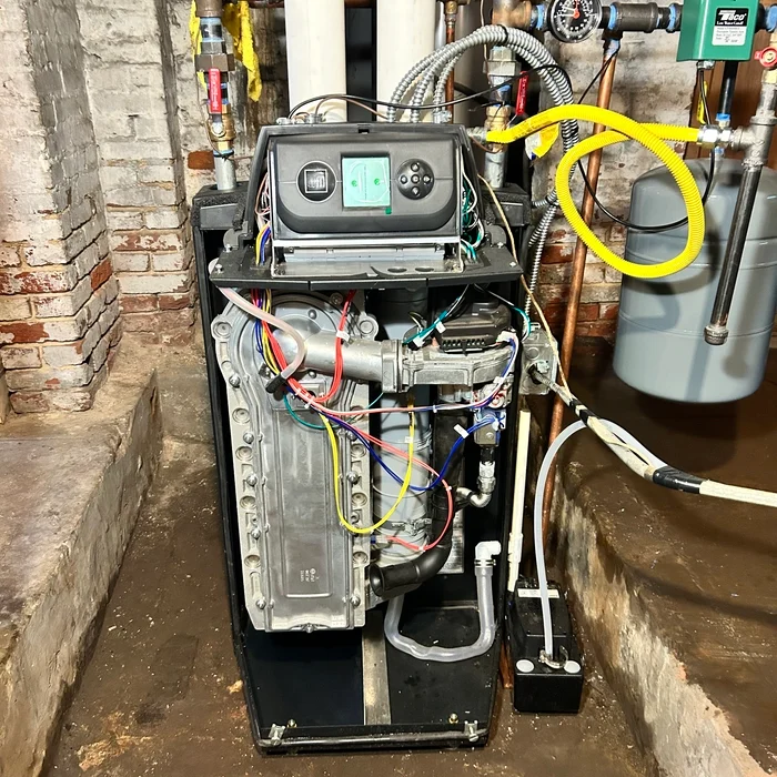 Replacement boiler in the same basement with its front cover removed and connections visible.