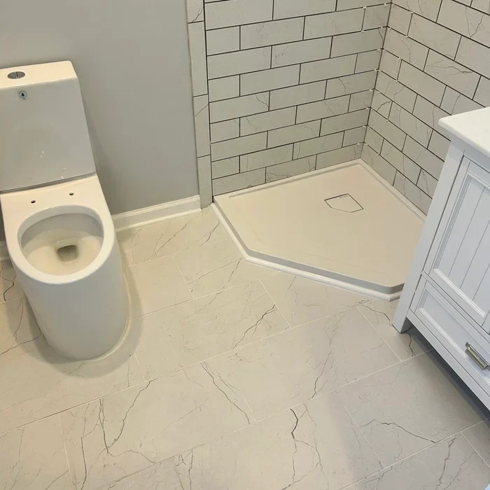 Toilet, corner shower base and white vanity in the same compact tiled bathroom.