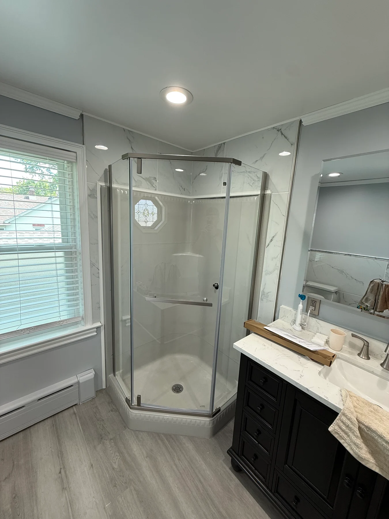 Clear-glass corner shower with a white base, pale wall panels and a dark vanity beside it.