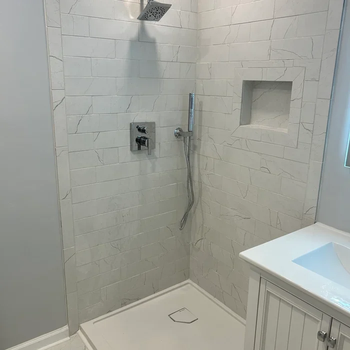 Tiled corner shower with a square overhead showerhead, handheld spray and recessed wall niche.