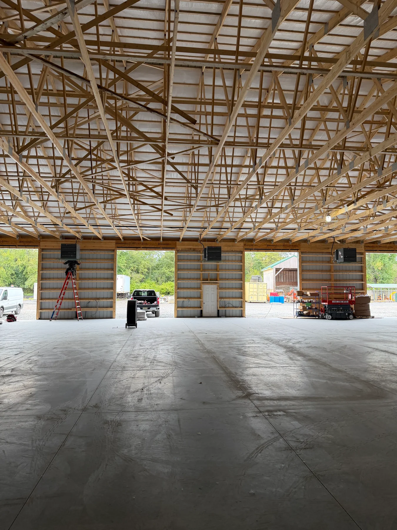 Suspended heaters and overhead gas piping in a warehouse with exposed timber roof trusses.