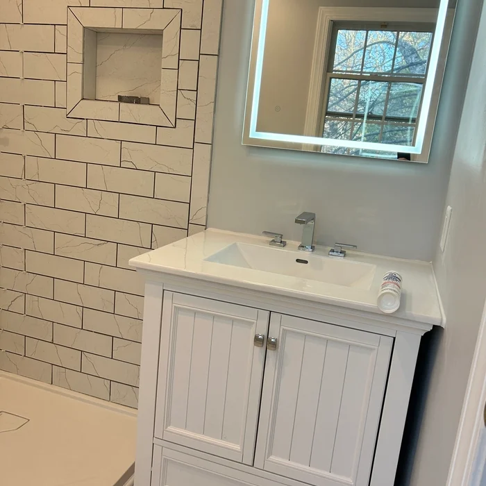 White bathroom vanity and three-piece chrome faucet beside the tiled shower niche.